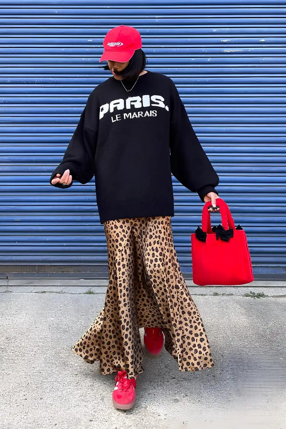 Seidenrock mit Leopardenmuster, kombiniert mit schwarzem oversized Hoodie, rotem Hut und Sneakers