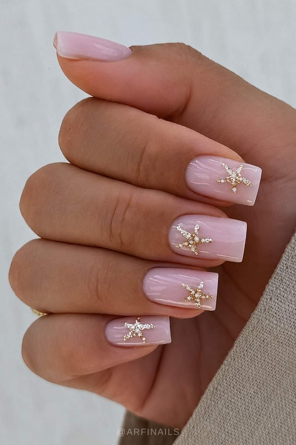 Milchig rosa Manikuere mit goldenen Seesternen