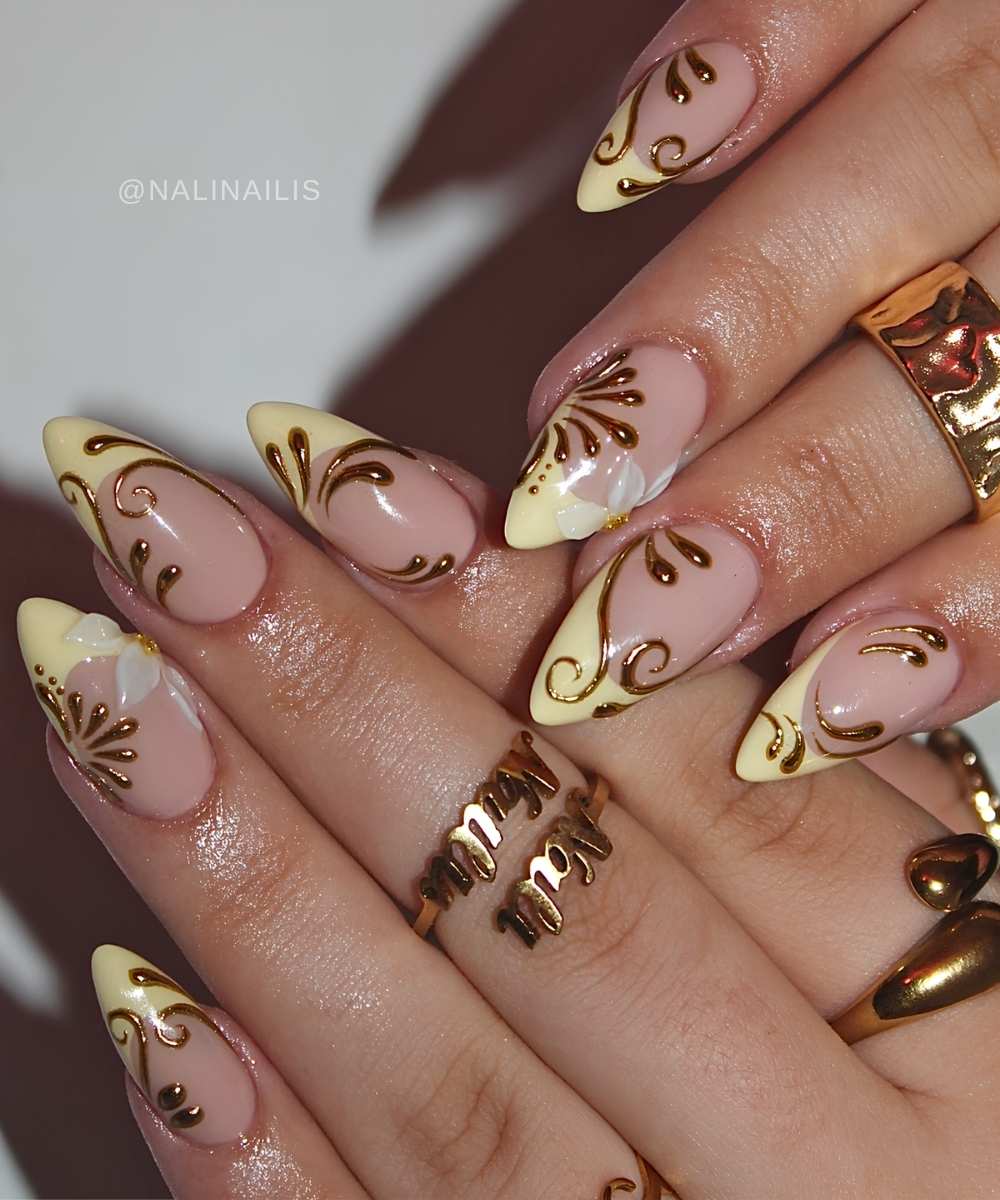 Gelbe French Manikuere mit goldenen Schnoerkeln und Blueten