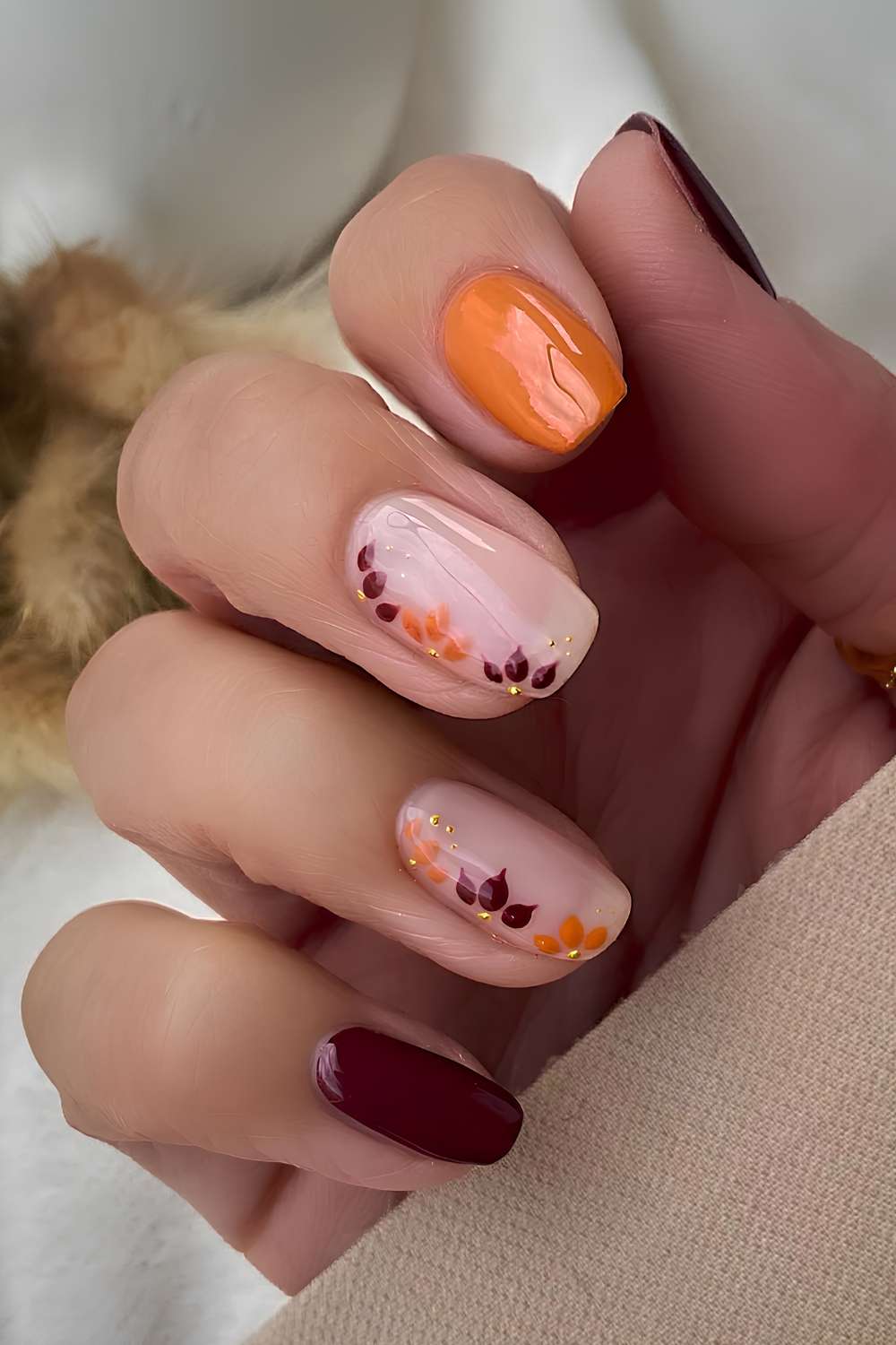 Bordeauxrote und orange Herbstnaegel mit Blumen